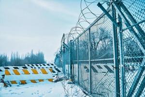 spinato filo recinto su confine con calcestruzzo strada blocchi su terra nel inverno. foto