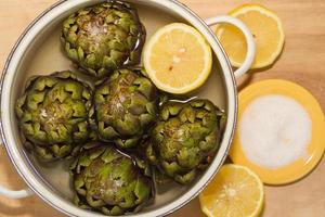 carciofi cucinato con Limone e sale nel il pentola con acqua foto