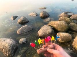 contento compleanno iscrizione fatto di vacanza candele nel il mani di un' uomo e un' donna di fronte il acqua di il oceano lago fiume foto