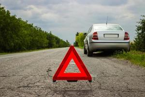 rosso triangolo di un' auto su il strada. auto avvertimento triangolo su il strada contro il città nel il sera. abbattersi di il auto nel cattivo tempo atmosferico. foto