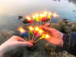 ardente contento compleanno iscrizione fatto di vacanza candele nel il mani di un' uomo e un' donna di fronte il acqua di il oceano lago fiume. concetto compleanno celebrazione nel natura, all'aperto foto