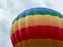 grande multicolore luminosa il giro arcobaleno colorato a strisce a strisce volante Palloncino con un' cestino contro il cielo nel il sera foto