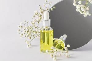 un' trasparente cosmetico bottiglia con siero o naturale olio per automedicazione sta a un' il giro specchio con un' gipsofila. biologico cosmetici. foto