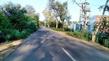 rurale nero pesca strada con rosso suolo strada nel il giungla circondato di verde alberi a indiano villaggio foto