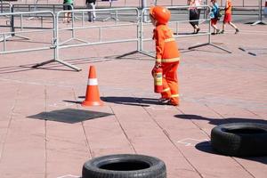 un' poco ragazza nel un scontroso resistente al fuoco completo da uomo corre con un' fuoco estintore per spegnere un' fuoco a un' concorrenza foto