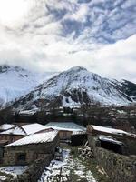 piccolo pietra case, edifici nel il villaggio su un' bellissimo montagna freddo inverno ricorrere con alto montagna picchi nebbia e neve coperto rocce per snowboard e sciare contro un' blu cielo foto