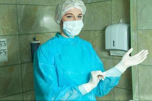 chirurgo donna nel un' accappatoio prepara respirazione maschera e latice guanti vestiti foto