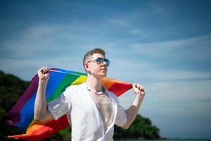 giovane gay uomo Tenere arcobaleno bandiere mentre in piedi su il spiaggia foto