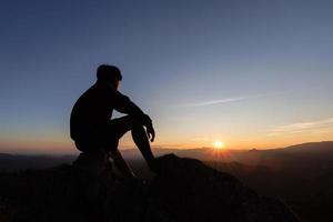 silhouette di triste uomo seduta solo su superiore di un' montagna a tramonto, depressione e solitudine. il concetto di fatica e oscurità. foto