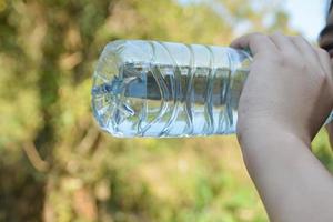 qualcuno potabile acqua un' plastica bottiglia. foto