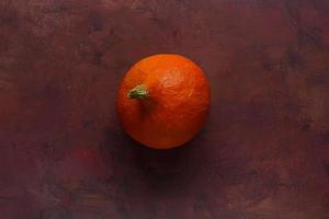 piccolo maturo arancia zucca su un' Borgogna rustico sfondo foto