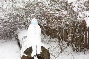 pupazzo di neve nel un' medico maschera - un' nuovo realtà, protezione a partire dal patologia, infezione, vita nel il covid epidemico. Da donna mani mettere su un' pupazzo di neve maschera. inverno famiglia all'aperto attività foto