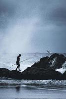 sydney, australia, uomo in piedi sulle rocce vicino al mare con una canna da pesca foto