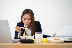 occupato e stanco donna d'affari mangiare spaghetti per pranzo a il scrivania ufficio e Lavorando per consegnare finanziario dichiarazioni per un' capo. oberati di lavoro e malsano per pronto pasti, bruciato concetto. foto