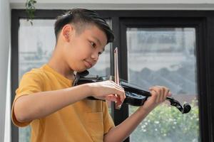 un ragazzino asiatico che suona e pratica lo strumento a corda musicale del violino contro in casa, concetto di educazione musicale, ispirazione, studente di scuola d'arte per adolescenti. foto