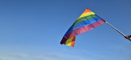 arcobaleno bandiera Tenere nel mano contro cielo blu sfondo, concetto per lgbt celebrazione nel orgoglio mese, giugno, in giro il mondo. foto