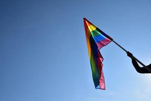 arcobaleno bandiera Tenere nel mano contro cielo blu sfondo, concetto per lgbt celebrazione nel orgoglio mese, giugno, in giro il mondo. foto