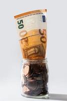 cinquanta Euro banconota dentro un' bicchiere vaso pieno di rame monete. foto