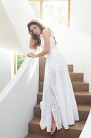 bellissima donna indossare bellissimo bianca vestito su un' scala dentro sua Casa foto