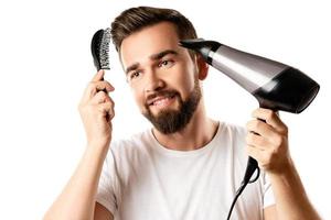 bello uomo è utilizzando capelli spazzola e asciugacapelli per il suo acconciatura foto