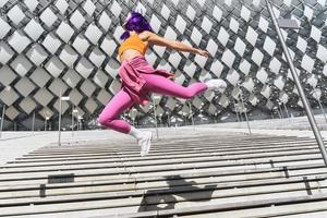 spensierato donna indossare colorato abbigliamento sportivo salto su il strada durante estate giorno foto