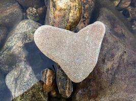 un' a forma di cuore pietra bugie su pietre sopra il acqua, orizzontale orientamento foto