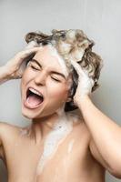 giovane bellissimo donna cantando e lavaggio sua capelli con shampoo foto