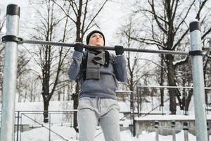 atletico donna fare pull-up su orizzontale bar durante all'aperto inverno allenarsi foto