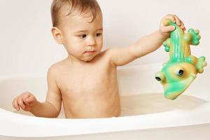 poco ragazzo giocando con gomma da cancellare coccodrillo mentre assunzione un' bagno. foto