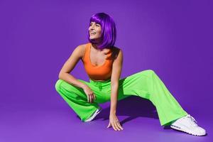 spensierato donna ballerino indossare colorato abbigliamento sportivo avendo divertimento contro viola sfondo foto