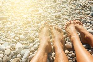 vicino su di di coppia piedi su il ciottolo spiaggia foto