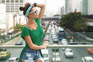 elegante modello indossare verde camicia e bandana è in posa su il ponte accanto autostrada foto