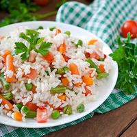 appetitoso salutare riso con verdure nel bianca piatto su un' di legno sfondo. foto