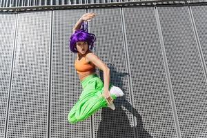 spensierato donna indossare colorato abbigliamento sportivo salto su il strada durante estate giorno foto