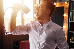 giovane uomo con microfono è cantando a voce alta a casa foto