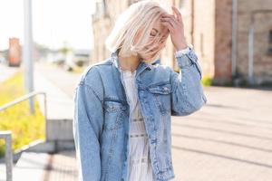 giovane bionda ragazza con spettinato capelli su un' città strada foto