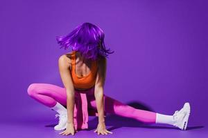 donna indossare colorato abbigliamento sportivo durante allungamento allenarsi contro viola sfondo foto