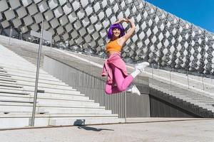 spensierato donna indossare colorato abbigliamento sportivo salto su il strada durante estate giorno foto