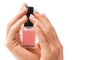 femmina mani con bellissimo francese manicure Tenere bottiglia di rosa chiodo polacco contro bianca sfondo foto