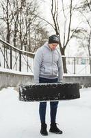 forte sportivo durante il suo formazione incrociata con un' pneumatico allenarsi durante nevoso e freddo inverno giorno. foto