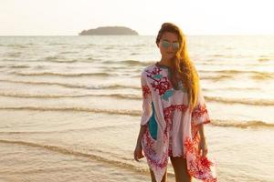 giovane bello donna indossare bellissimo vestito è a piedi di il mare riva foto