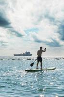 giovane maschio surfer equitazione in piedi paddleboard nel oceano. foto