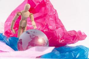 burattino di legno tocca il globo di cristallo sul sacchetto di plastica e si sente preoccupato e deve proteggere la terra. i rifiuti di plastica traboccano il mondo. concetto di riscaldamento globale e cambiamento climatico. foto