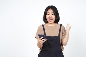 utilizzando smartphone con sì celebrazione gesto di bellissimo asiatico donna isolato su bianca sfondo foto