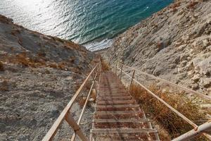 un' metallo scala principale giù per il robusto, incontaminata costa di il mare. foto