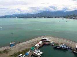 molti navi, Barche, crociera fodere nel il porta e acqua su il tropicale mare caldo estate ricorrere con palma alberi contro il blu cielo e alto montagne foto