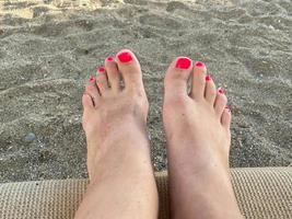 femmina gambe, piedi con un' bellissimo rosso pedicure su il sfondo di sabbia su vacanza su il spiaggia nel un' caldo tropicale orientale Paradiso nazione meridionale ricorrere foto