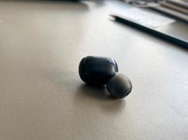 un' piccolo nero plastica senza fili Bluetooth auricolare per ascoltando per musica bugie su il tavolo foto