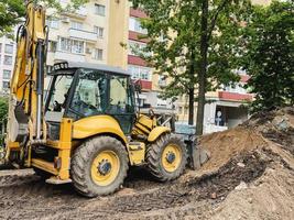 luminosa, giallo scavatrice scava un' buco nel il sabbia. costruzione macchinari. affidabile strada e fossa costruzione veicolo unità attraverso sabbia e le foglie pneumatico brani foto