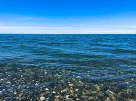 bellissimo multicolore il giro pietre su il mare, fiumi, laghi, stagno, oceano e bollente acqua con onde su il roccioso spiaggia di un' tropicale caldo ricorrere su il orizzonte e cielo. verticale Visualizza foto